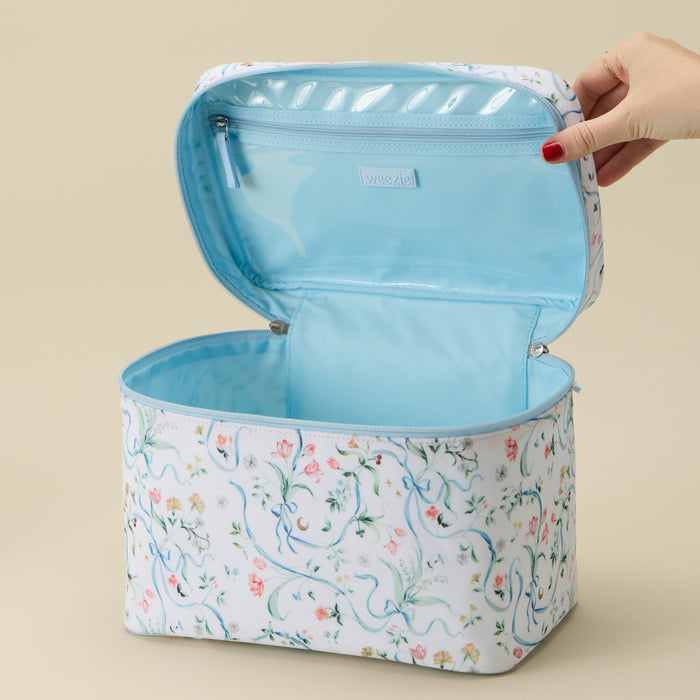 A rectangular zippered cosmetic bag with a white exterior covered in a delicate blue and pink floral vine pattern, shown open with a hand holding the inner flap. The interior is lined in light blue.