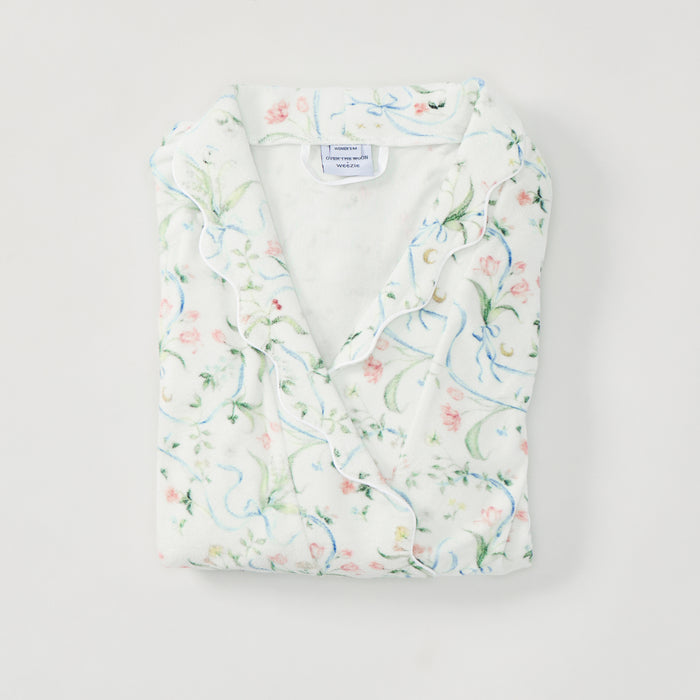 A folded white cotton pajama shirt with a delicate pastel floral and vine print, featuring ruffled trim along the collar and front placket, laid flat on a light gray background.