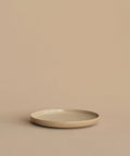 A Pacific Salad Plate, round and beige, rests on a matching surface with a beige background, forming a minimal and neutral scene.