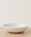 The Pacific Serving Bowl, crafted from white stoneware in Portugal, is shown empty on a light wooden surface with a plain off-white background.