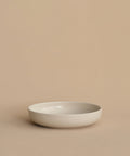 A simple, round, shallow white Pacific Soup Bowl is displayed on a beige surface against a matching background, highlighting its minimalistic, pattern-free elegance.