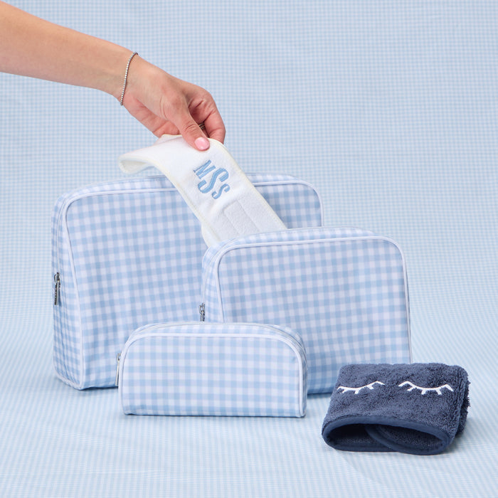 A set of three light blue gingham toiletry bags in small, medium, and large sizes with an embroidered headband on top.