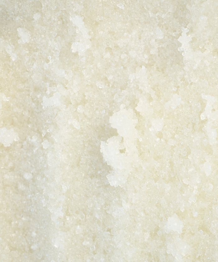 Close-up of coarse, white granules in Perfecting Body Scrub, featuring an uneven crystalline texture—ideal for exfoliating and hydrating skincare rituals.