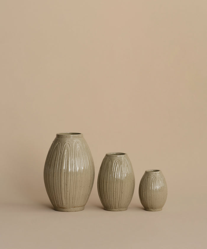 Three ribbed ceramic vases in a light beige-gray glaze, arranged by size against a solid warm beige background.