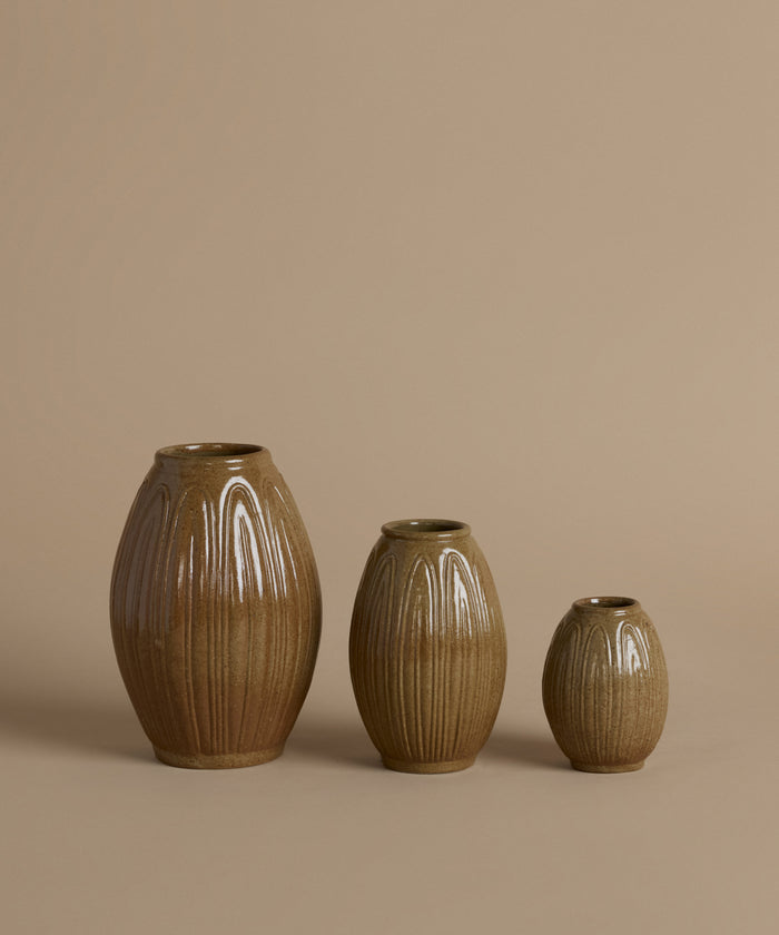 Three ribbed ceramic vases in graduated sizes with a glossy brown glaze, arranged against a solid beige background.