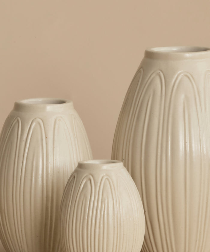 Three ribbed ceramic vases in a warm cream-beige color, arranged against a solid beige background.