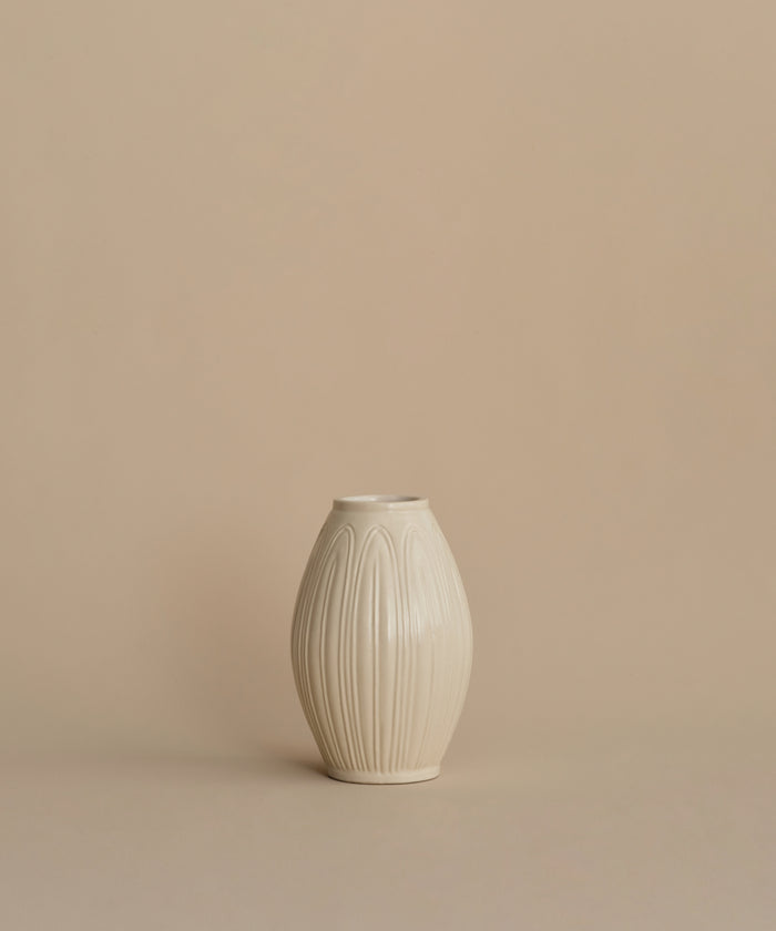 A small cream-colored ceramic vase with a textured vertical ribbed pattern, centered against a solid beige background.