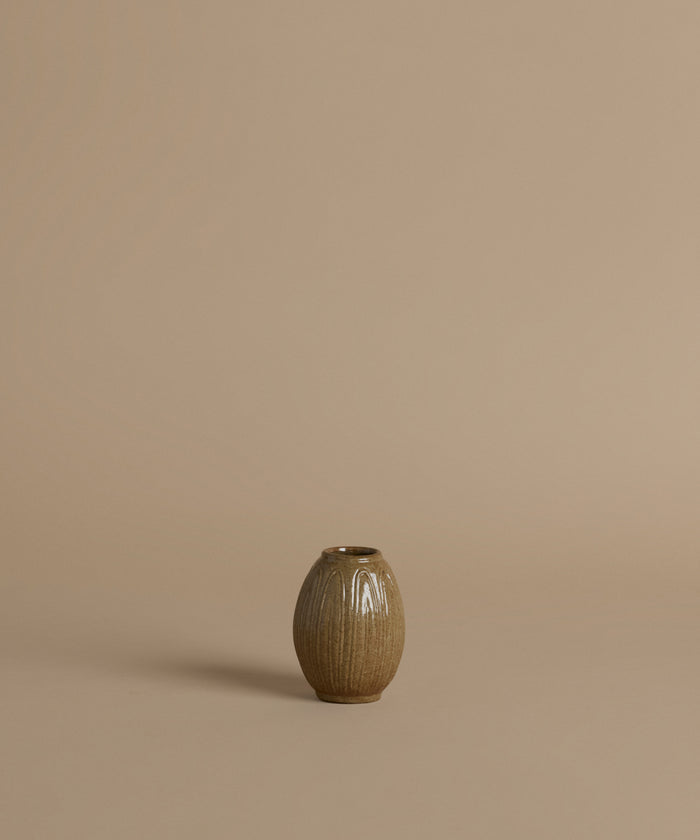 A ribbed ceramic vases with a glossy brown glaze, arranged against a solid beige background.