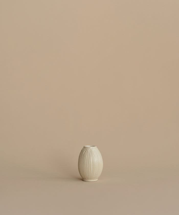 A small cream-colored ceramic vase with a ribbed, lotus-like texture, centered against a solid, warm beige background.
