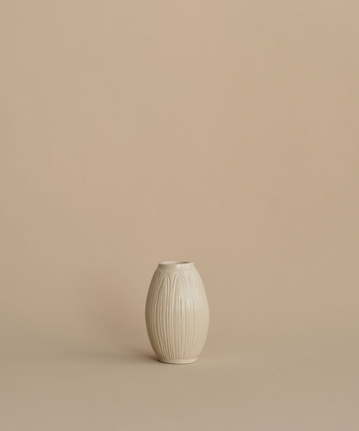 A small cream-colored ceramic vase with a ribbed, lotus-like texture, centered against a solid, warm beige background.