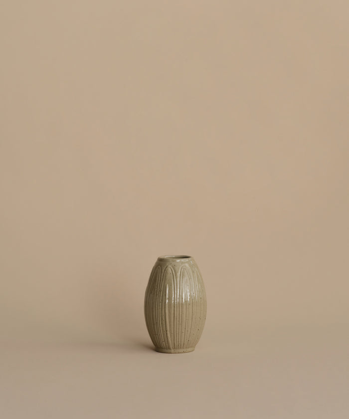 A small ribbed ceramic vase in a muted sage green-gray glaze, centered against a solid warm beige background.