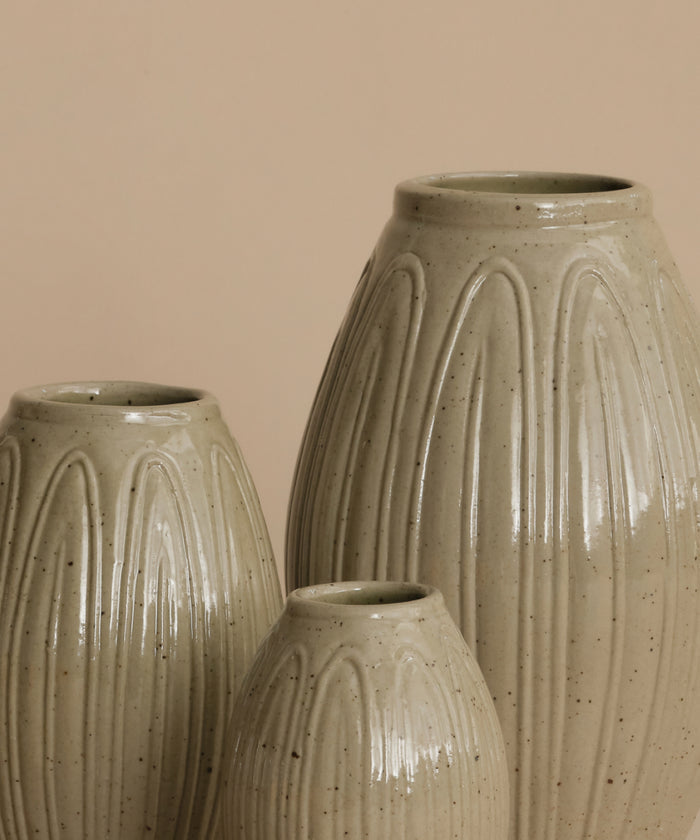 Three ribbed ceramic vases in a speckled light beige glaze, arranged against a solid warm beige background.