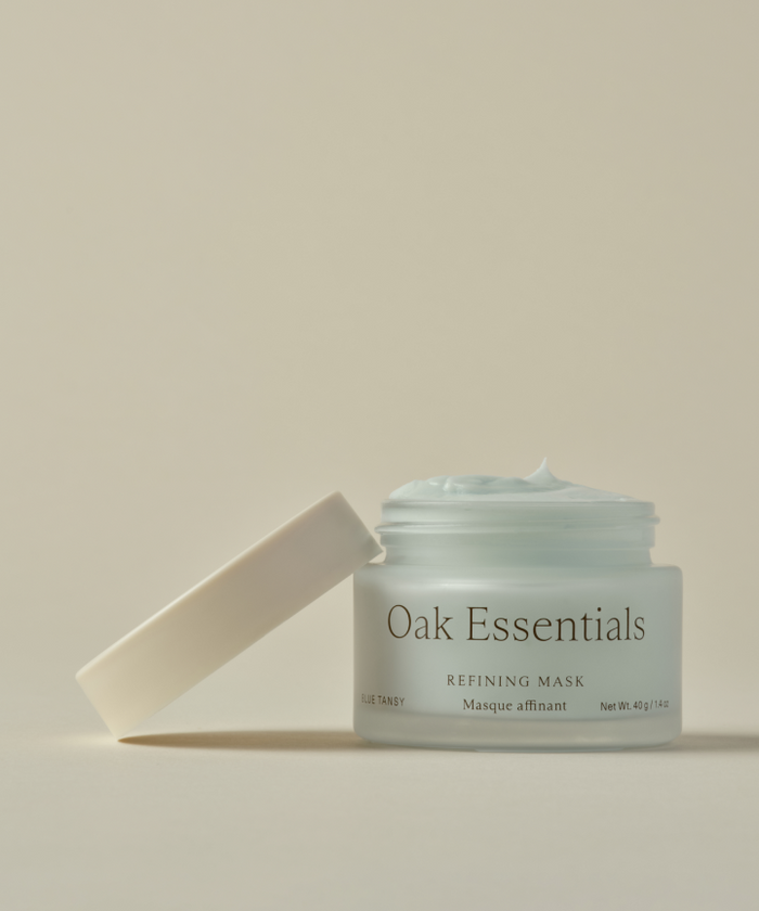 A light blue Refining Mask sits in an open glass jar labeled “Refining Mask” on a neutral background, with the lid resting at an angle beside it.