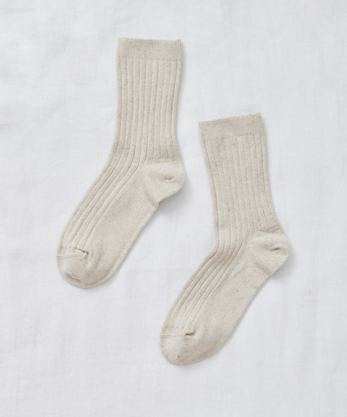 A pair of light beige Rib Socks, perfect for all seasons, is laid flat on a white fabric background with the toes facing opposite directions.