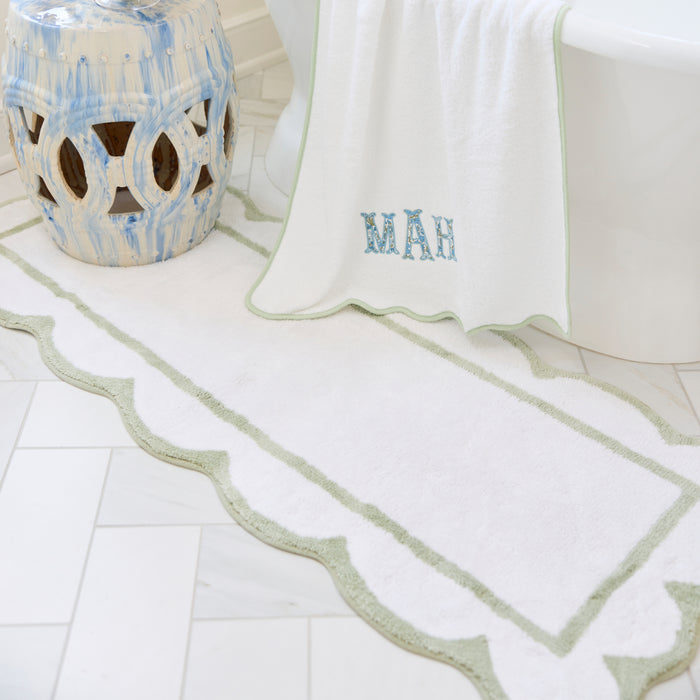 Laurel green scalloped bath runner with crisp white trim on a tiled bathroom floor.