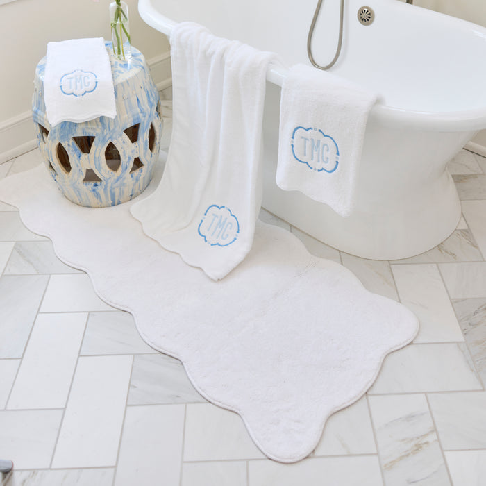 Crisp white scalloped bath runner with white trim resting on a tiled bathroom floor.