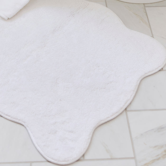 Crisp white scalloped bath runner with white trim resting on a tiled bathroom floor.