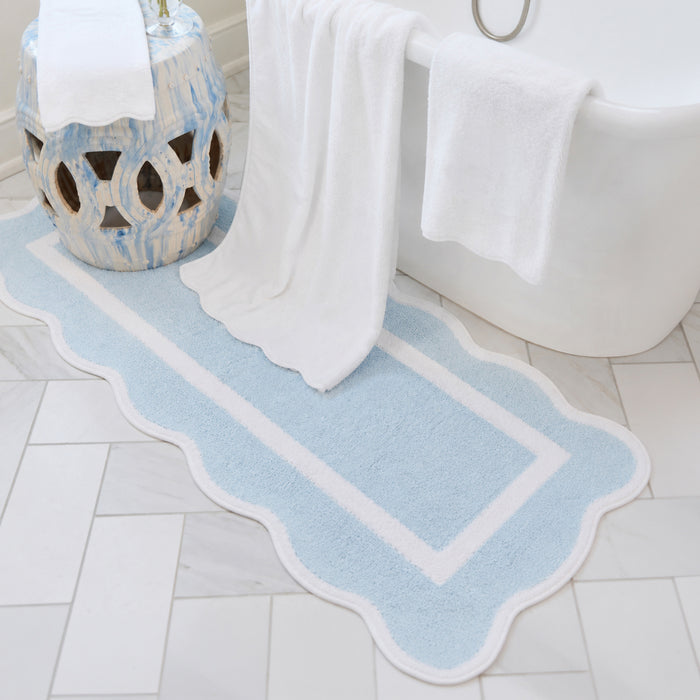 Mist blue scalloped bath runner with white trim on a tiled floor next to a white tub.