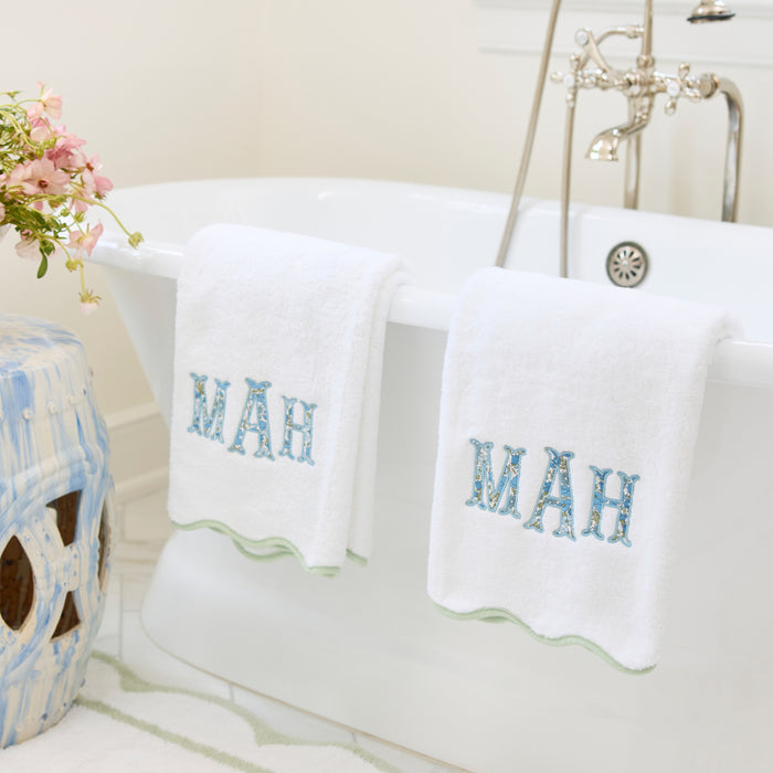 White scallop bath towels with matcha green piping and MAH applique monogram draped on a tub.