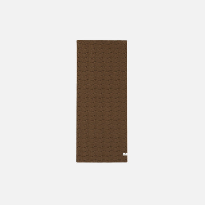 Brown plush cotton towel with subtle wavy pattern on white background.