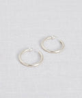 The Small Clara Hoops, crafted in sterling silver with post backings, are displayed on a light, textured fabric surface.
