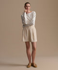 Woman wearing a striped shirt and beige shorts against a beige background