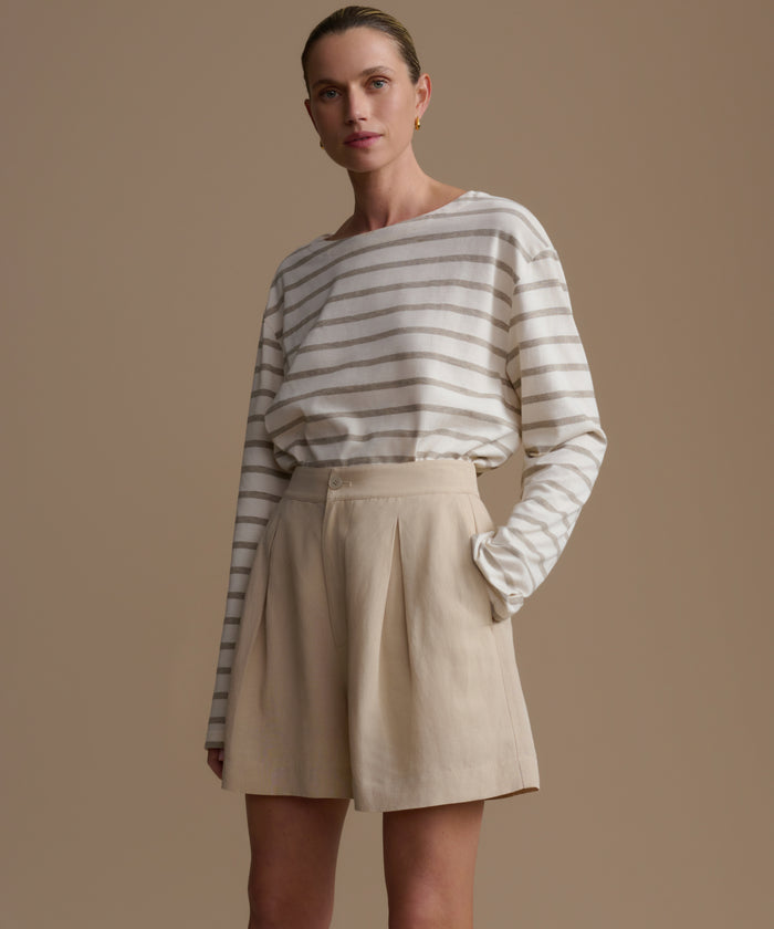 Woman wearing a striped shirt and beige shorts against a brown background