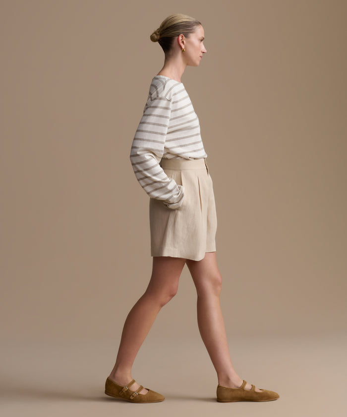 Woman wearing a striped shirt and beige shorts against a beige background
