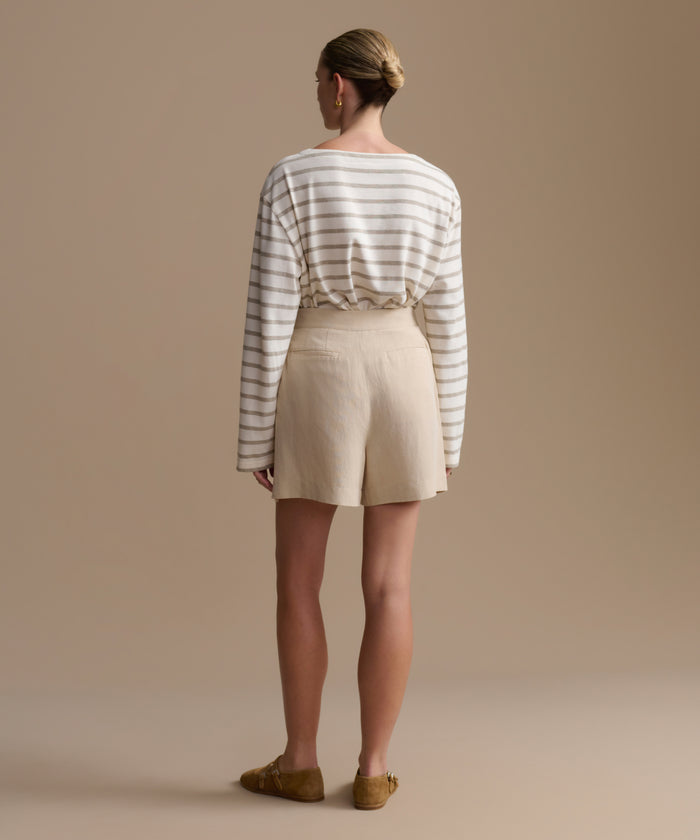 Woman wearing a striped shirt and beige shorts against a beige background