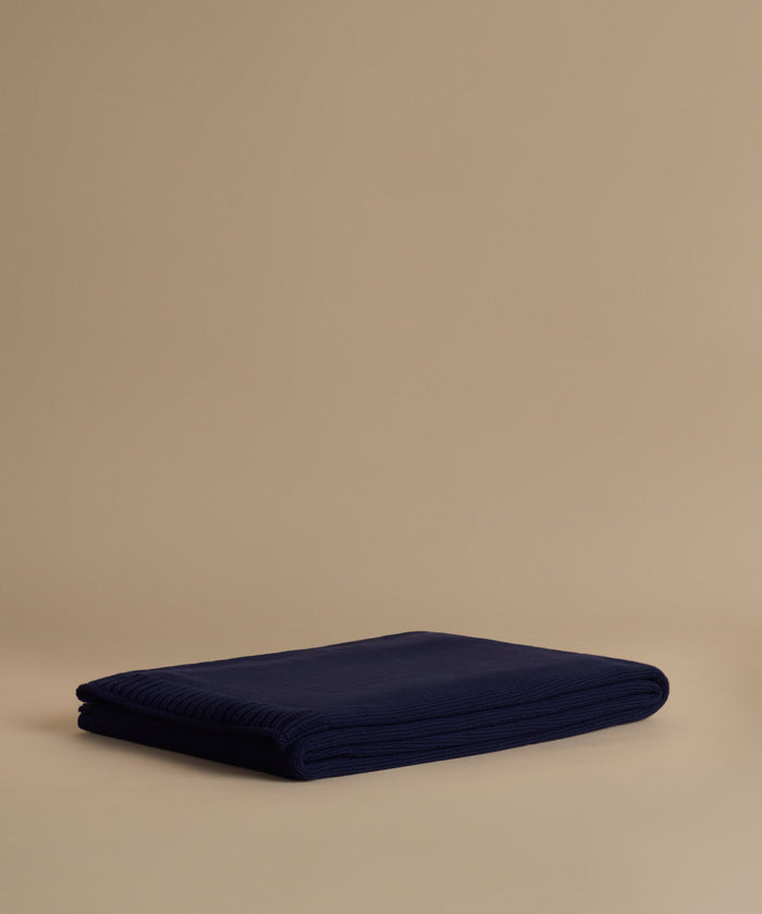 A folded navy blue ribbed knit blanket or throw is displayed on a warm beige studio background.