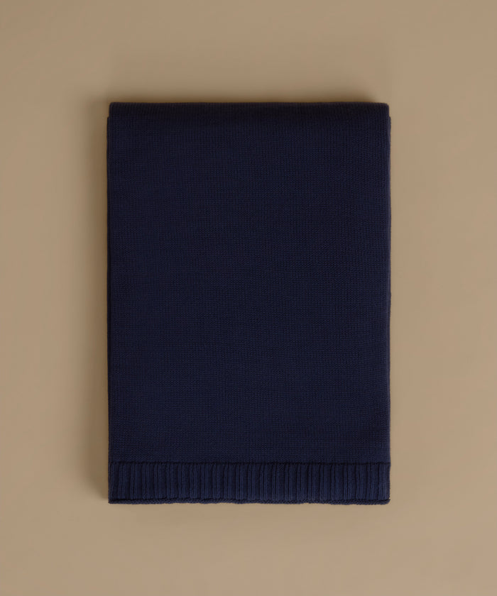 A folded navy blue knit blanket with a ribbed border, displayed flat against a solid beige background.