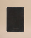 The Suede Passport Holder in black features subtle edge stitching and is displayed on a light beige background—an elegant touch for your travel essentials.