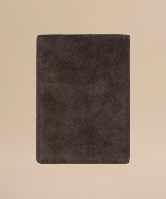 The Suede Passport Holder, a travel essential in dark brown with a soft, textured finish and subtle embossed text near the bottom, is centered on a light beige background.