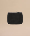 The Suede Pouch is a small black suede accessory with a zippered closure and minimalist design, perfect for use as a compact pouch or passport holder, pictured on a plain beige background.