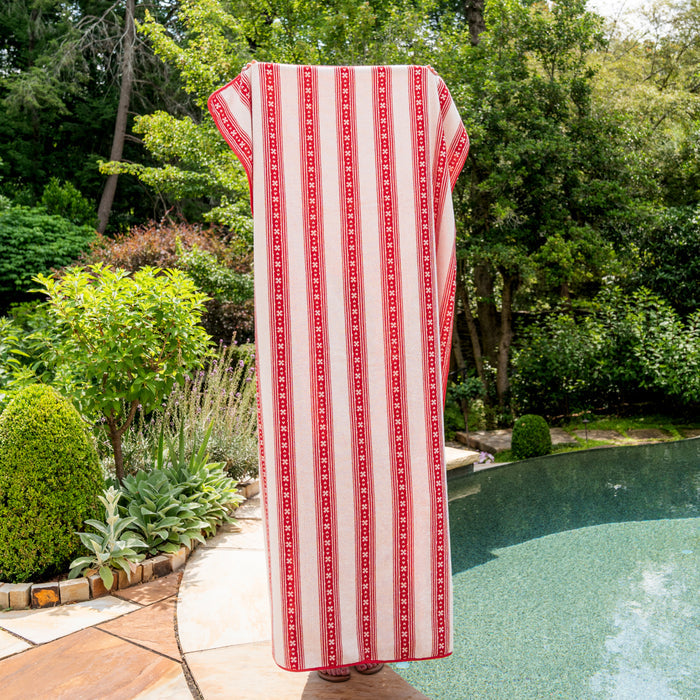 Red and white striped towel draped over a chair by a pool with greenery in the background