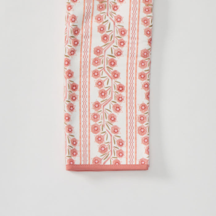 A folded kitchen towel featuring a pink and peach floral climbing vine pattern with a solid pink border.