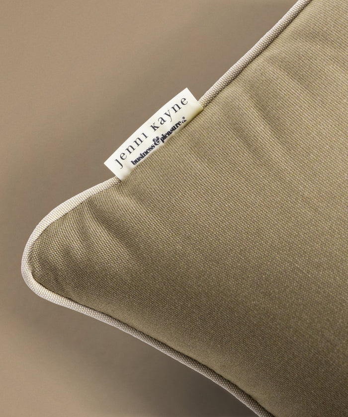 Close-up of a green pillow with a Jenni Kayne label on a beige background