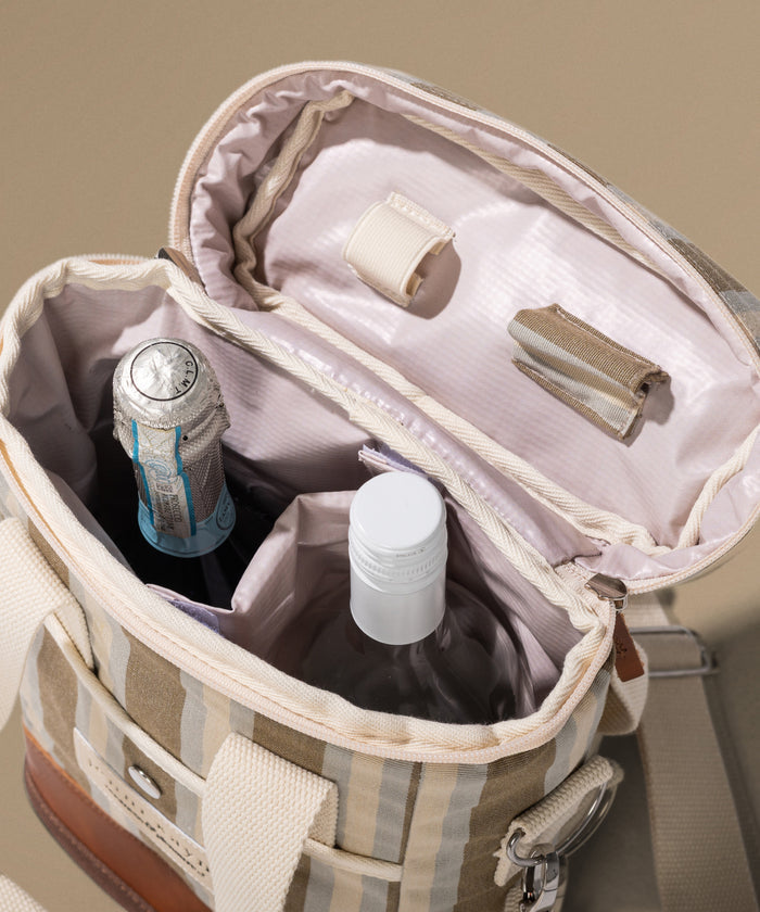 Open beige travel bag with a bottle and other items on a neutral background
