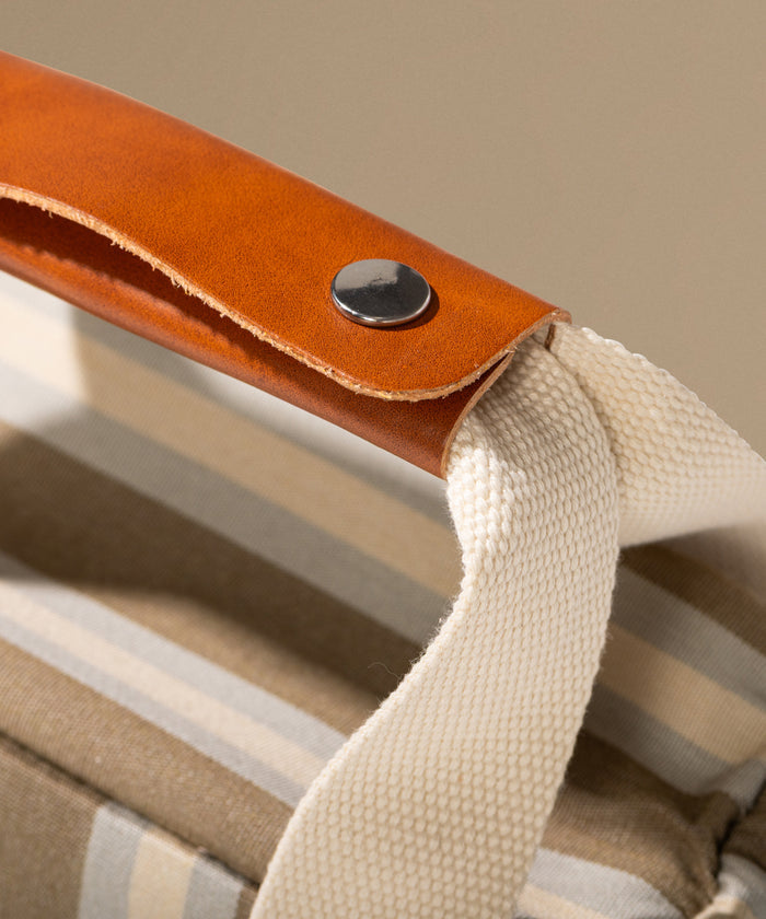 Close-up of a leather handle with a button on a striped bag.