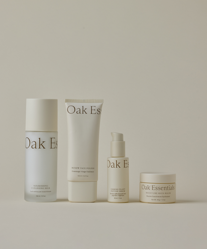 The Youthful Skin Routine by Four Oak Essentials features four skincare products—a cleansing milk, face polish, hydrating serum, and moisture balm—arranged in a row against a light beige background, all in minimalist white packaging.