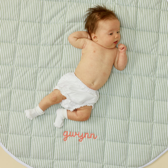 Baby lying down on a green striped tummy time mat with the name gwynn embroidered in pink.