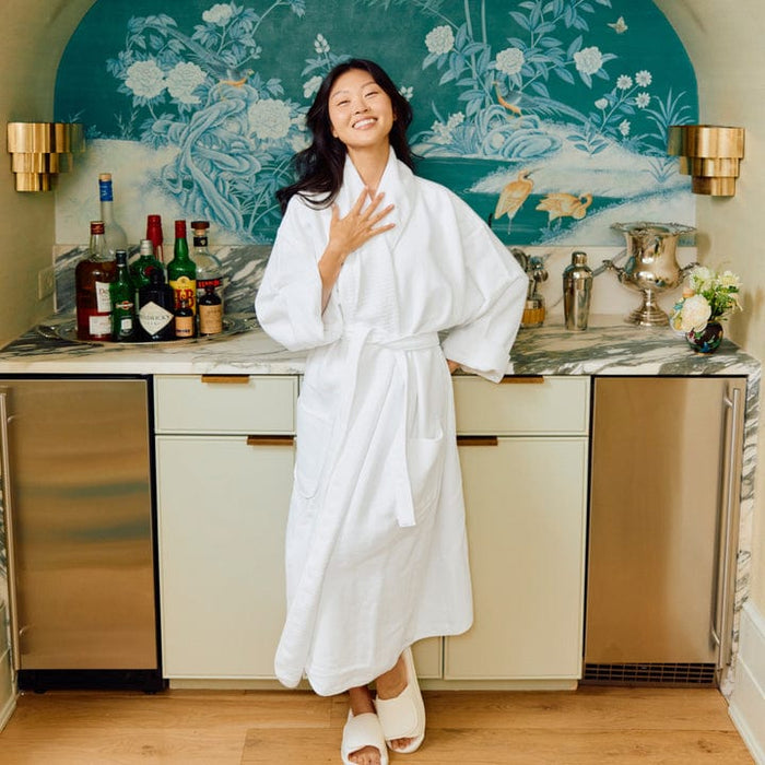 Woman in a white robe standing in a kitchen with a decorative wall and bar setup.