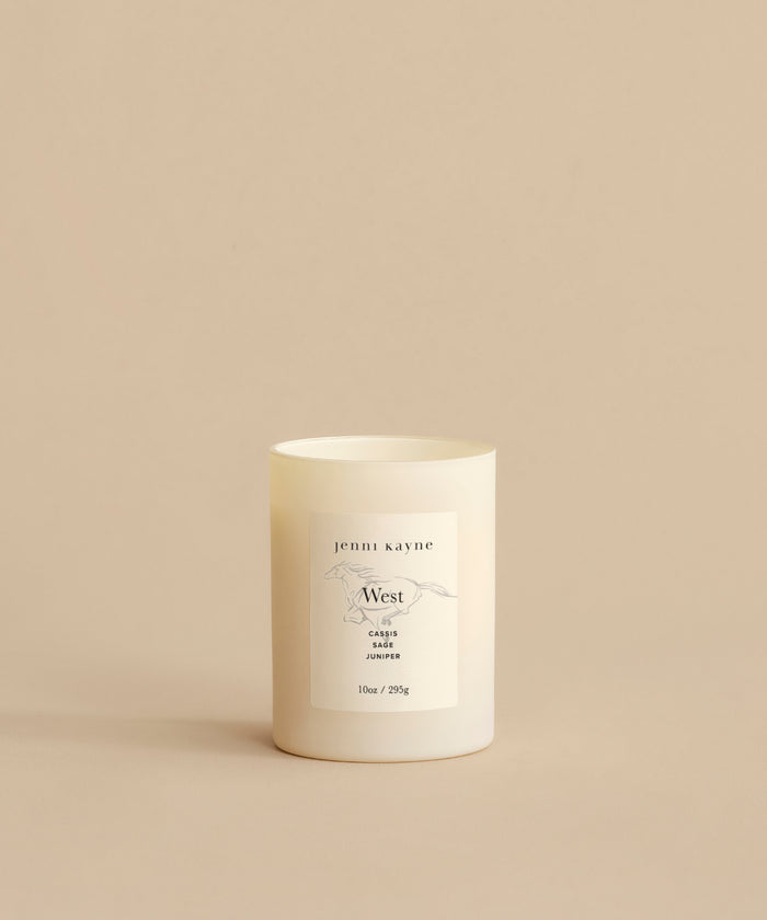 A West Glass Candle with a minimalist label sits on a beige surface and background, featuring simple text and line art to evoke the California-inspired scent.