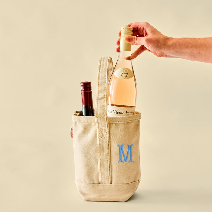 Hand placing a bottle of rosé into a canvas wine tote featuring a blue M monogram.
