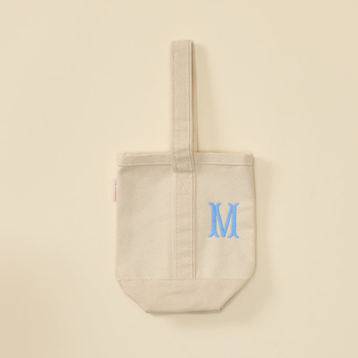 Cream canvas wine tote bag with a single strap and light blue embroidered letter M.