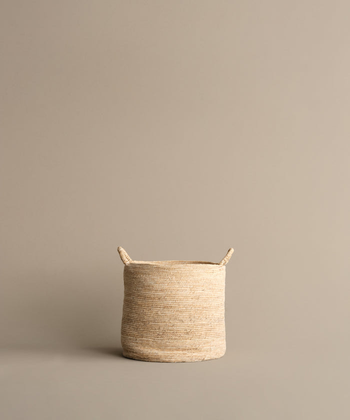 The Woven Storage Basket, featuring two small handles, rests on a neutral beige background. Its light color and stylish design make it an ideal solution for home storage needs.